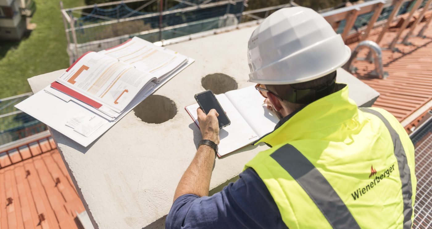 Urban roofer taking notes holding iPhone and writing in an urban location wearing hard hat and safety jacket, Fast Forward Commercial Excellence