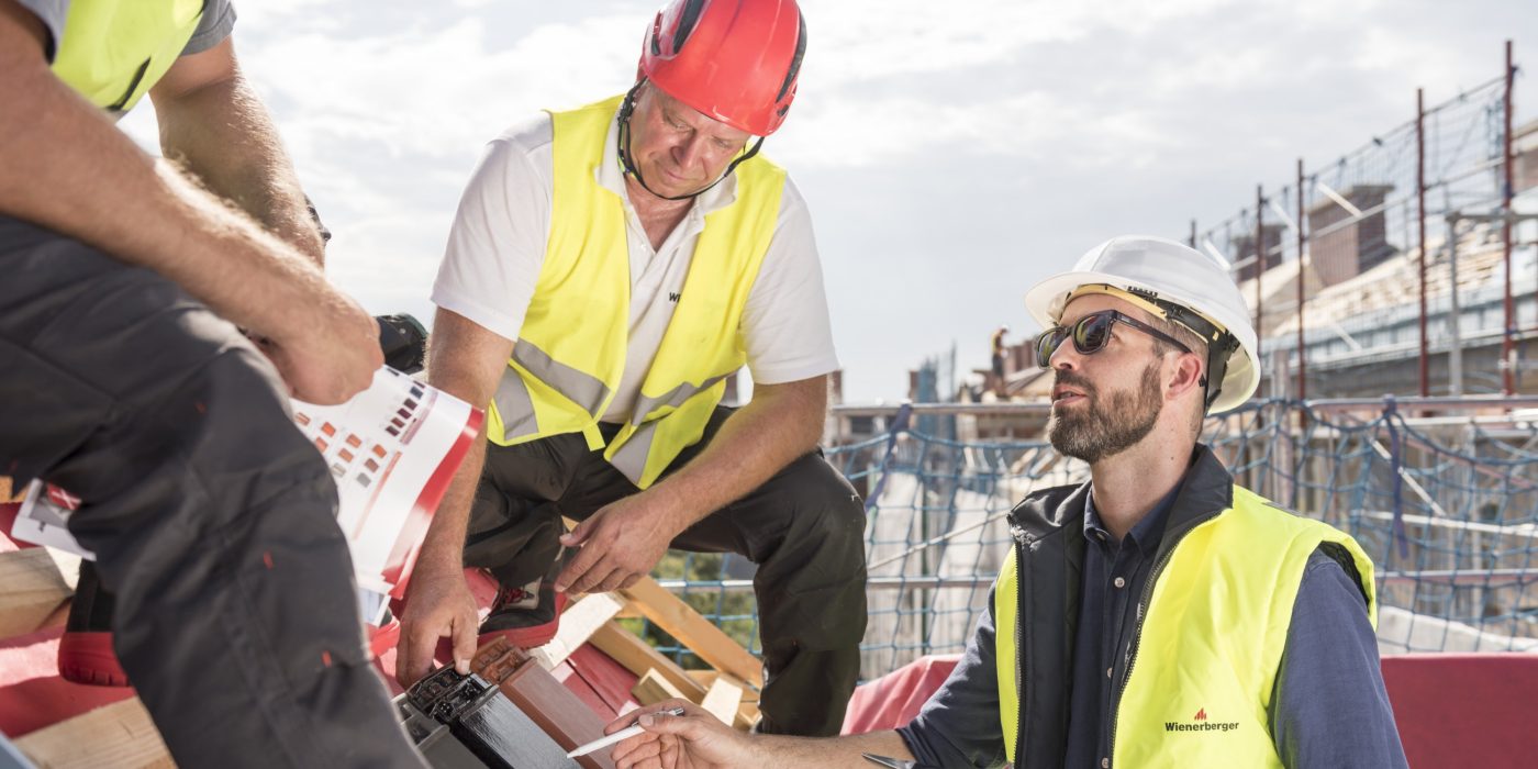 Product manager explaining product advantages to urban roofers wearing safety jackets and hard hats