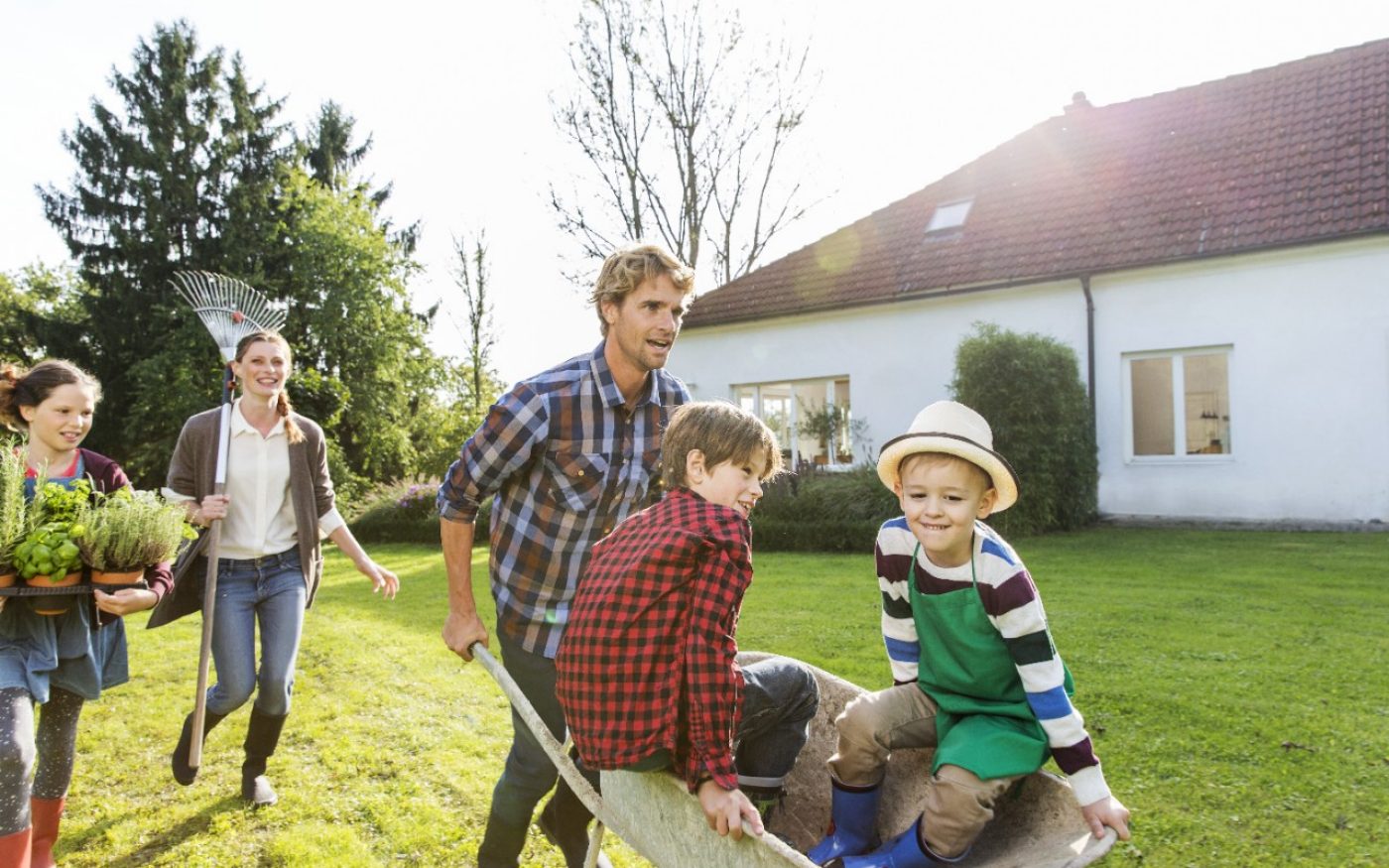 Man pushing two boys in wheelbarrow in front of single family house
