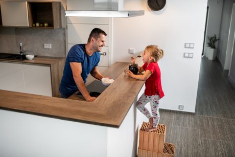 Holčička (dítě) stojící na cihlách u baru v kuchyni dívající se na svého tatínka