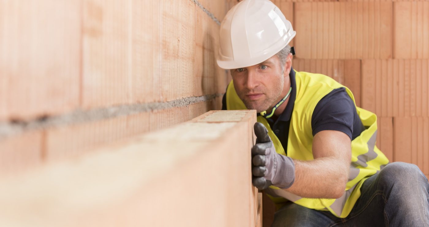 Construction worker checking alignment of mineral-wool filled clay block