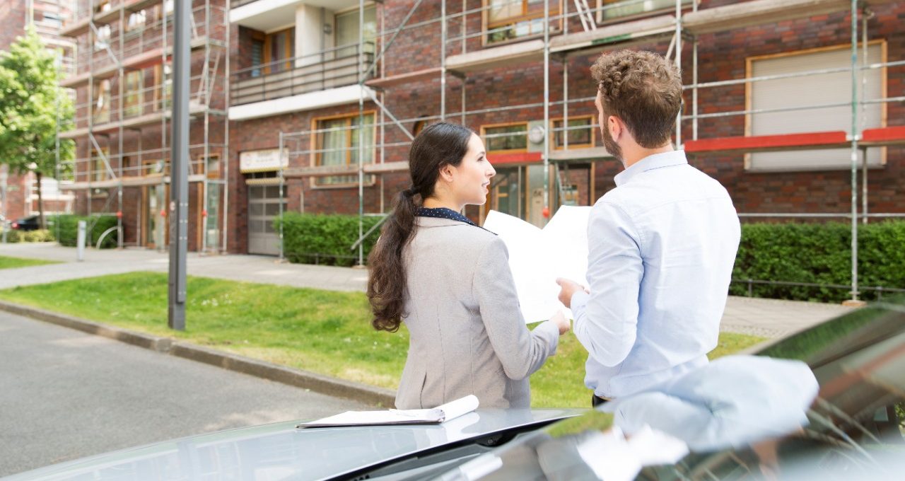 Business people talking about urban housing estate project in front of a brick building which is covered in scaffolding