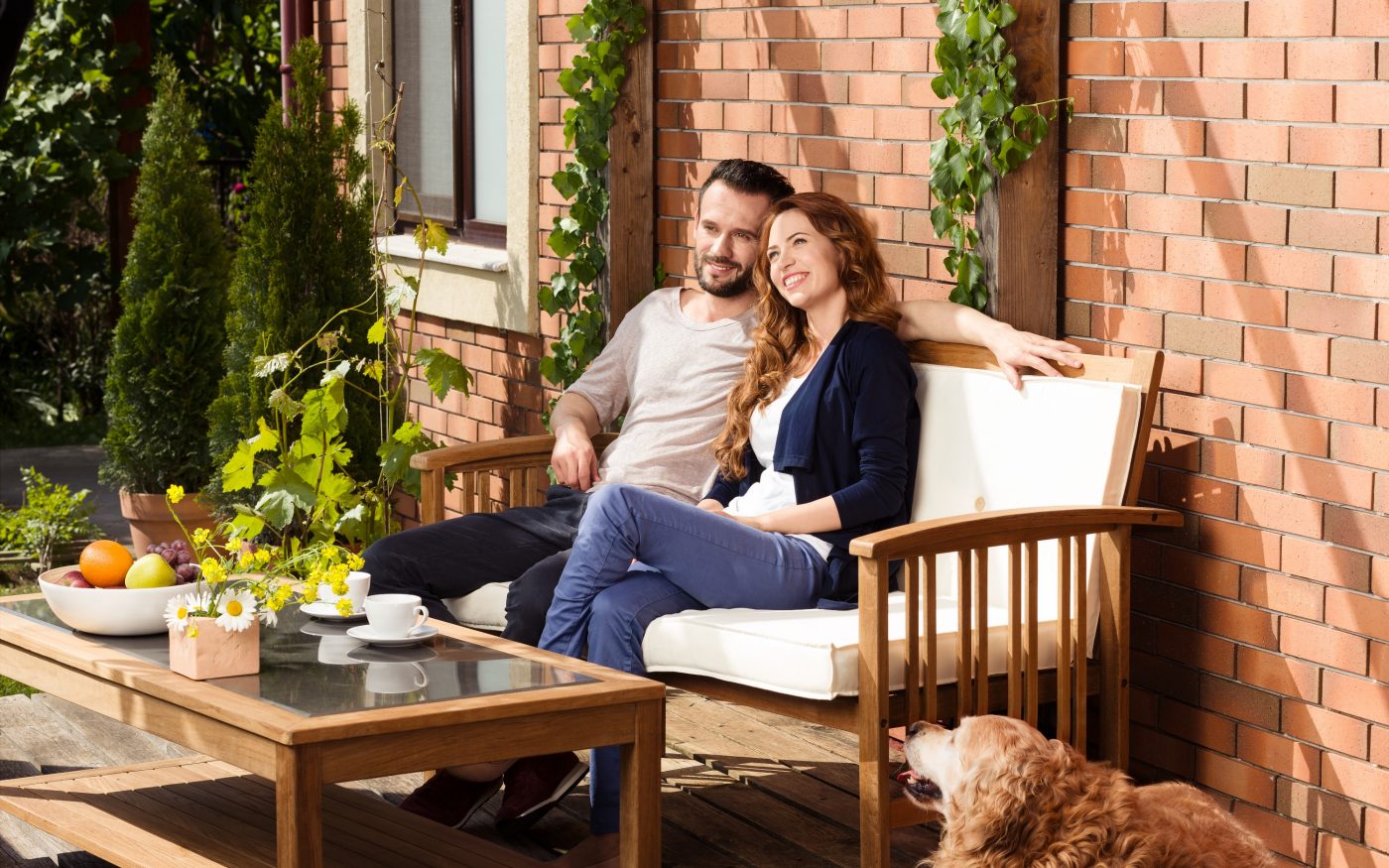 Man and woman sitting on garden bench in front of brick-lined façade