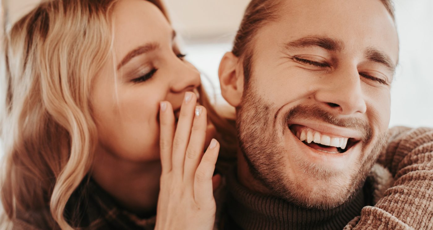Love is in the air. Close up portrait of happy woman whispering on ear something pleasant to her beloved laughing hipster man while embracing him