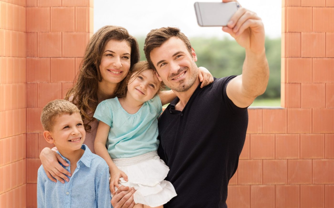 Parents with two kids taking a selfie with mobile phone inside new built house in front of bare clay block walls