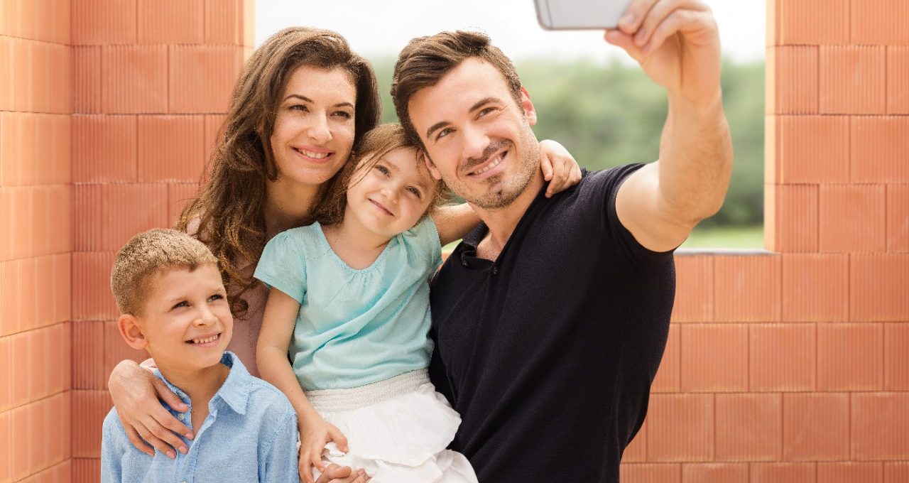 Parents with two kids taking a selfie with mobile phone inside new built house in front of bare clay block walls