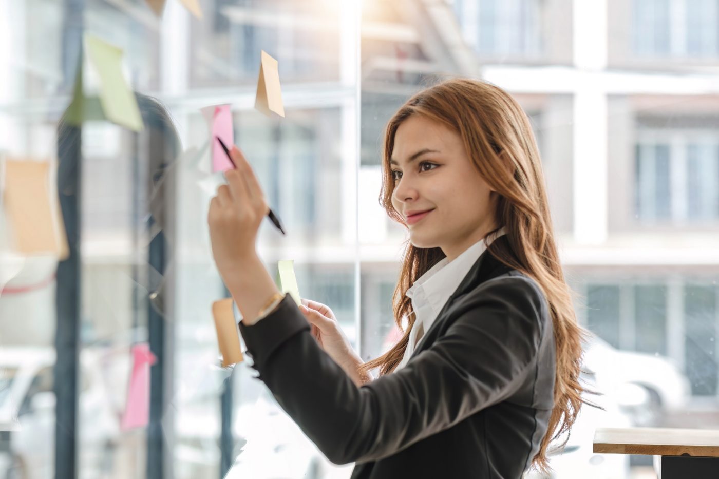 A beautiful young Asian female marketing assistant looking at the sticky note on a glass wall. ideas, notes, memo board
