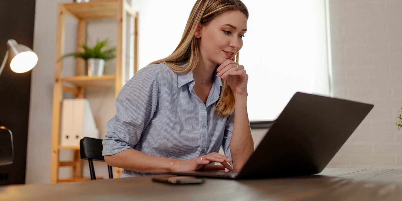 Close up photo of young smiling designer working on laptop at home office.