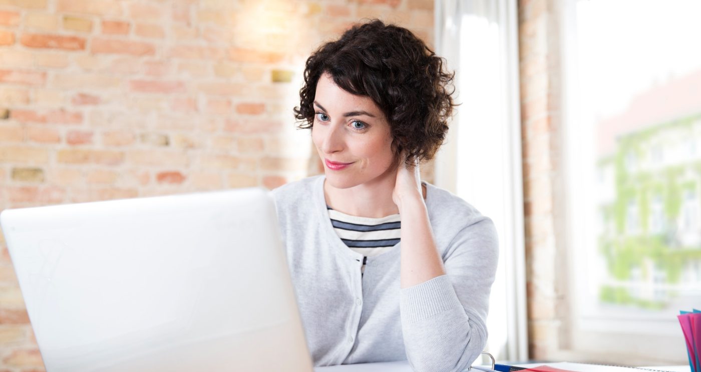 Woman looking at computer screen in front of brick-lined wall