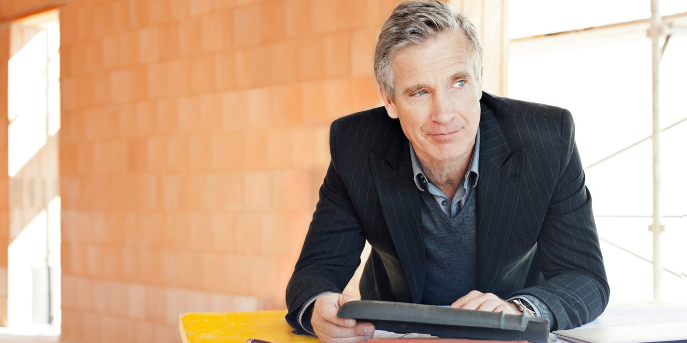 Man in suit comparing roof tiles in unfinished building surrounded by bare brickwork