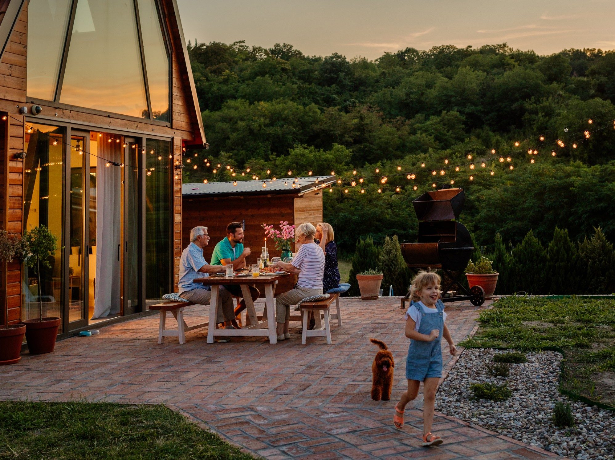 Young adult and senior couple sitting at the dining table in the backyard while little girl is playing beside them with her dog