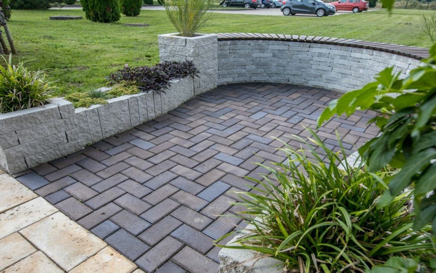 Semmelrock opločnici u tamno smeđe-sivim tonovima s uzorkom riblje kosti i Semmelrock polukružni zidni blok - uređena vanjska terasa s ukrasnim zelenilom