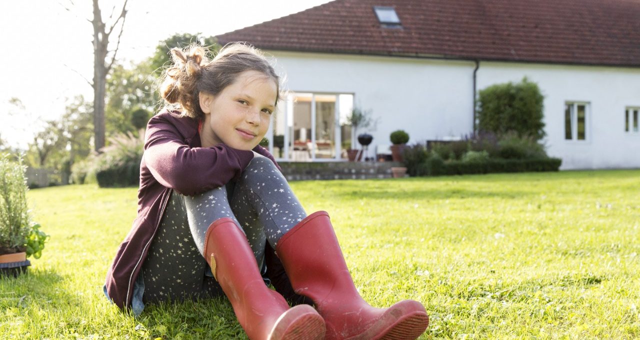 Girl sitting in the grass single family house in the background