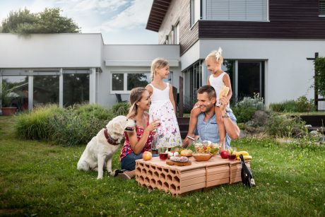 Rodina se psem sedící před domem na zahradě v popředí stropní vložky Miako jako stolek pro piknik