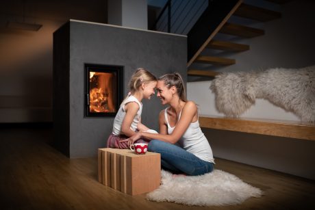 Žena maminka sedící s dítětem u teplého krbu v popředí cihla Porotherm T Profi